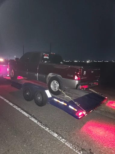 A truck loaded on the flatbed lit by the trailer lights at night