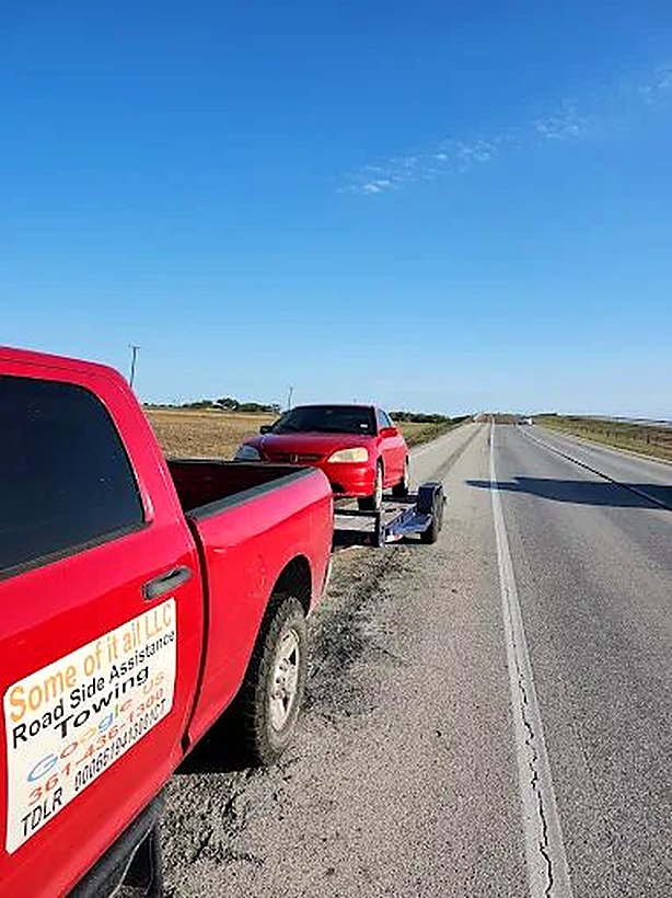 The red Some Of It All service truck towing a vehicle down the highway